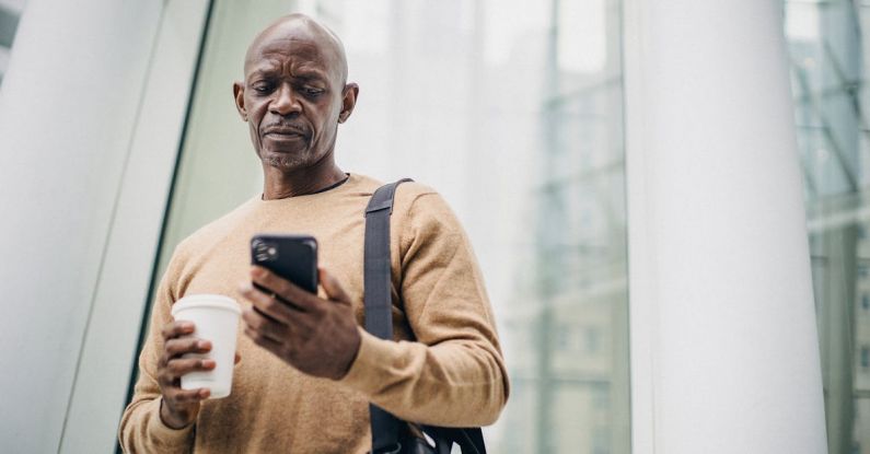 Energy Management - Focused mature black man chatting on smartphone during coffee break on street