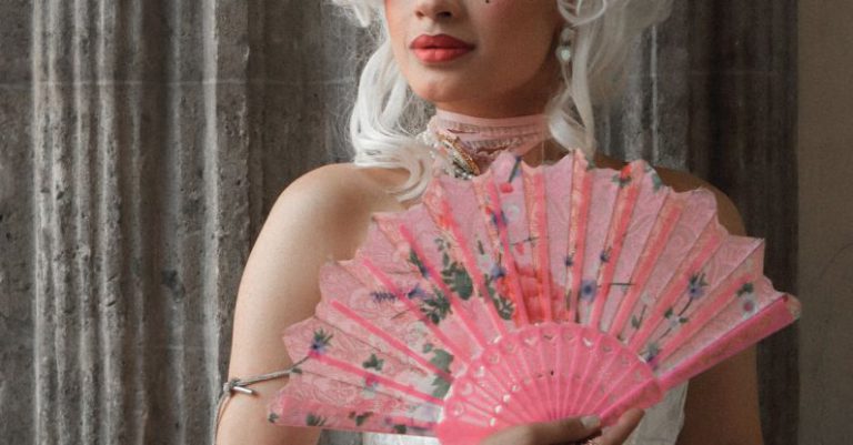 Sources Of Inspiration - A woman in a pink dress holding a fan