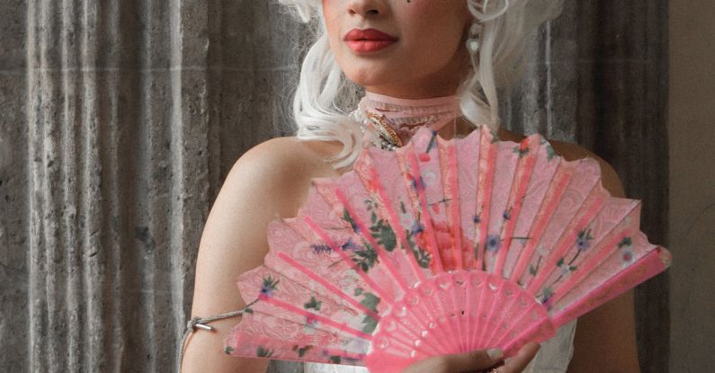 Sources Of Inspiration - A woman in a pink dress holding a fan