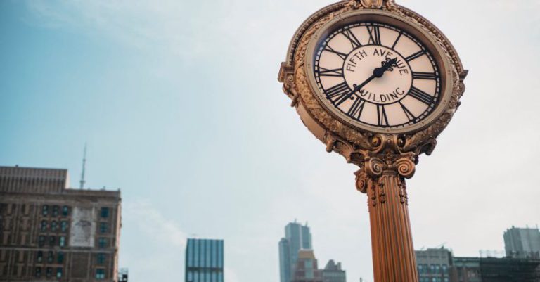 Time Blocking - From below of aged metal clock tower located in city center with high towers